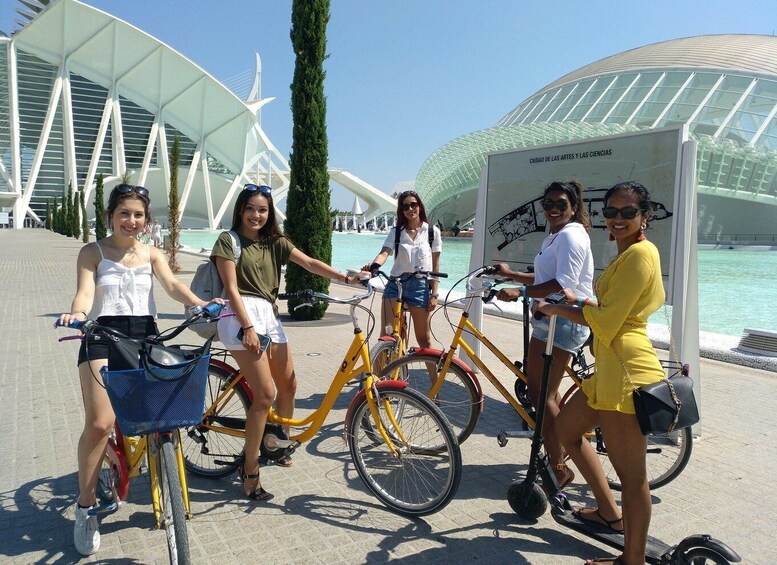 A group of people with bicycles and an electric scooter in front of a modern architectural structure with a glass dome. 3