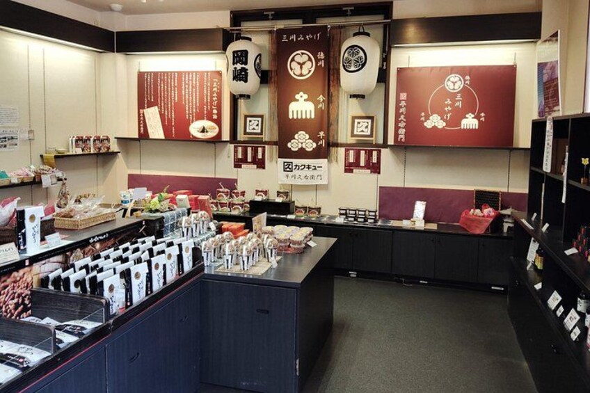 A Japanese-themed restaurant interior with a counter displaying various food items, a menu board, and decorative elements like lanterns and wall art. 3