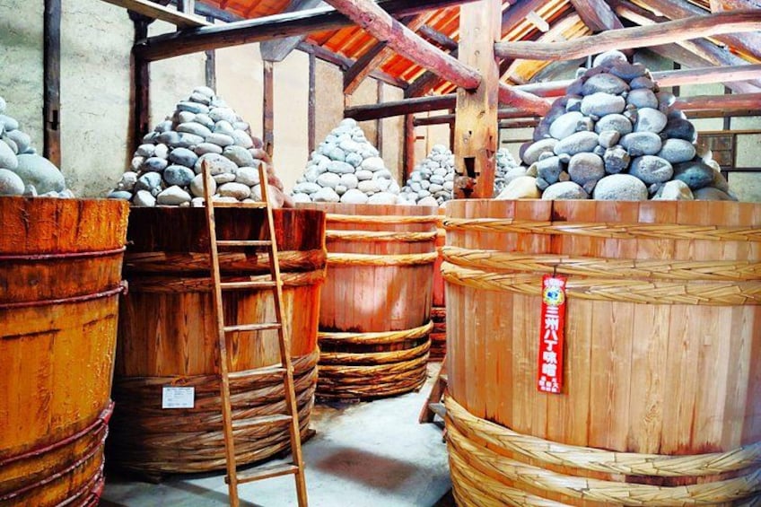 Wooden barrels stacked in a rustic setting, a ladder leaning against one barrel, and a sign with Chinese characters. 1