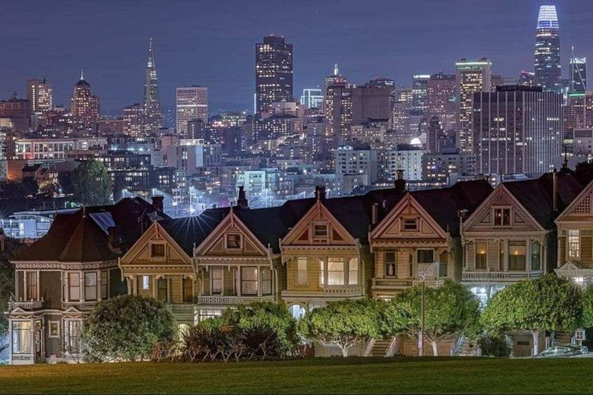 A city skyline at night with illuminated buildings and a row of historic houses in the foreground. 3