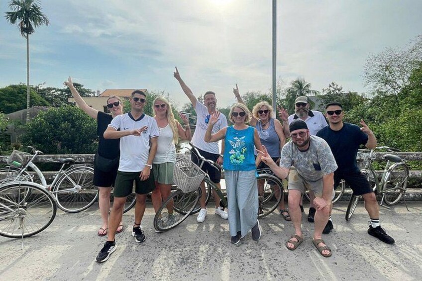 A group of people posing with bicycles on a bridge with palm trees in the background. 1