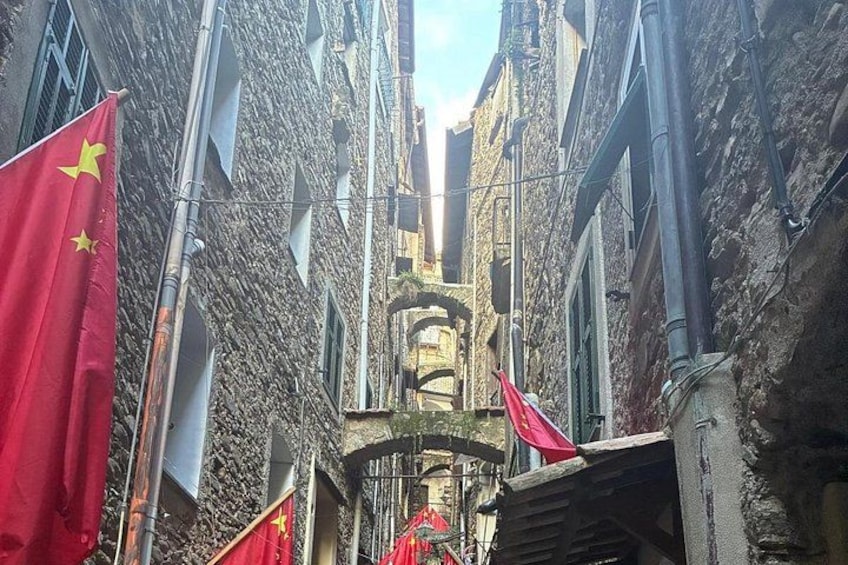 Una calle estrecha con edificios de piedra, banderas rojas y un campanario. 2