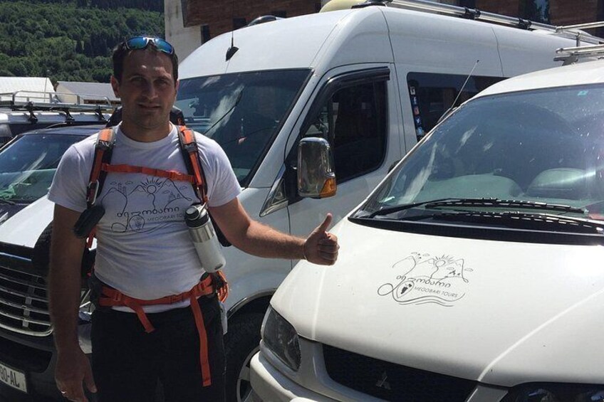 A person standing next to a white truck with a logo, wearing a white t-shirt and carrying a backpack. 2