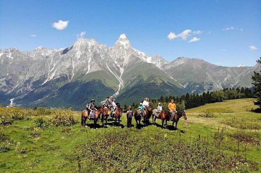 A group of people on horseback in a grassy field with a mountain range in the background. 5
