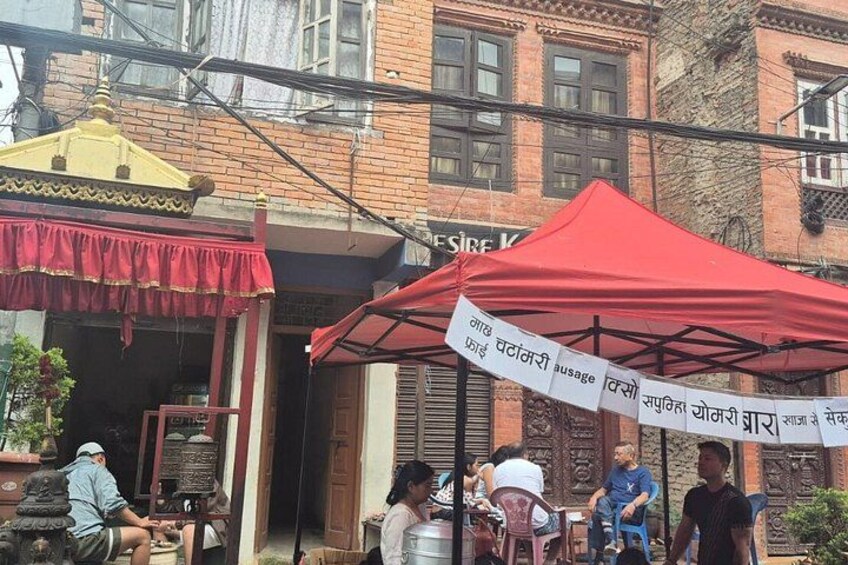 A red canopy with a sign, a brick building, and people sitting outside. 4