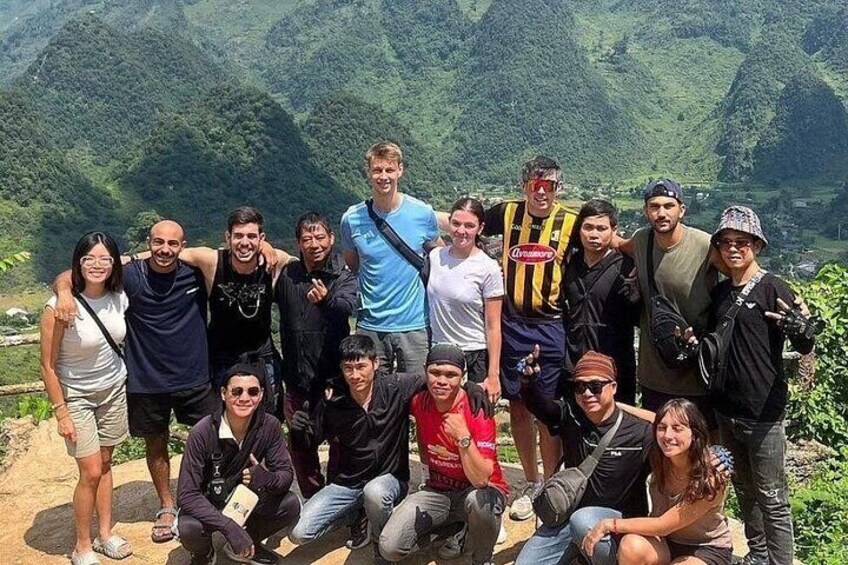 A group of people posing on a mountain trail with lush greenery and hills in the background. 4