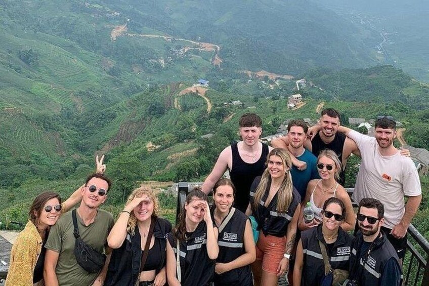 A group of people posing on a mountain ridge with a view of terraced fields below. 4