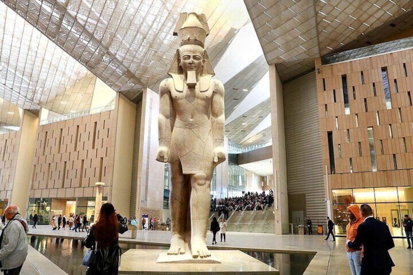 Une grande statue de l’Égypte ancienne, exposée dans un bâtiment moderne doté d’un plafond de verre et de murs à motifs. 1