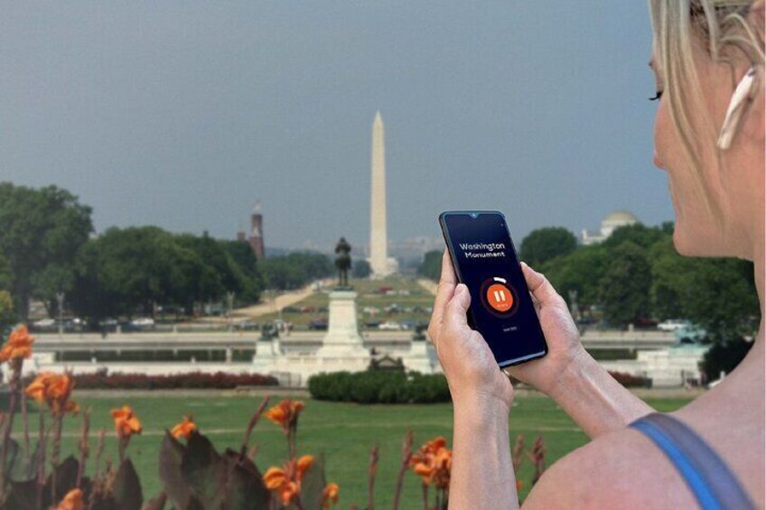 A person holding a smartphone with a Washington Monument app, with the monument in the background. 3
