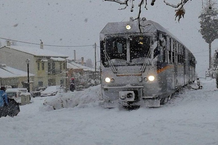 A snow-covered train moving through a snowy landscape with houses and trees in the background. 5