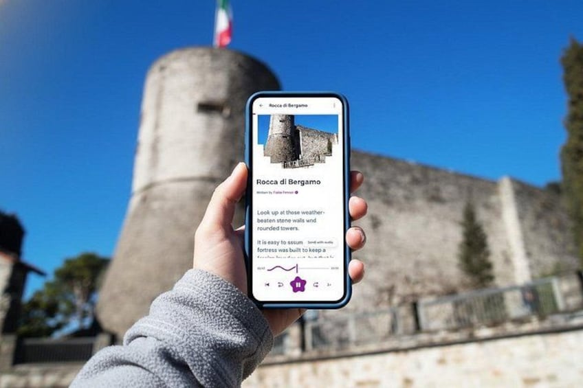 A hand holding a smartphone with a photo of Rocca di Ersamo. 1