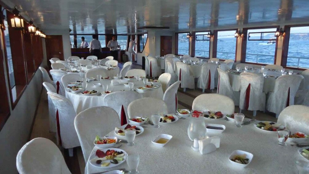 A dining area on a boat with tables set for meals, white chairs, and a view of the water. 2