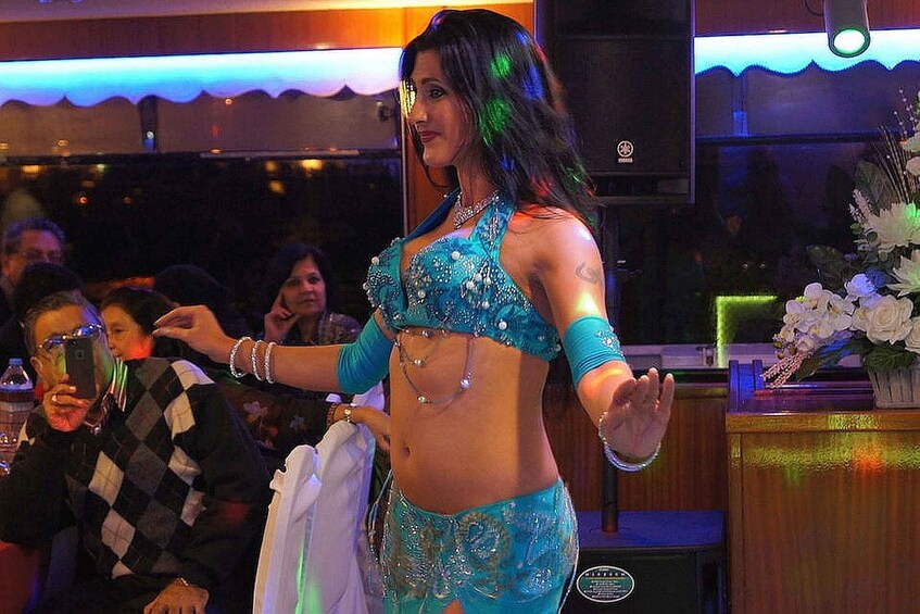 A person in a blue belly dance costume performing in a dimly lit venue with a crowd in the background. 5
