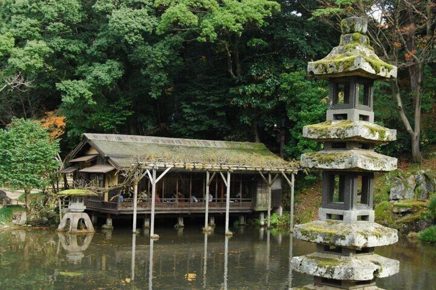 Un pavillon japonais traditionnel, situé au bord d’un étang, entouré d’une végétation luxuriante et agrémenté d’une lanterne en pierre. 5