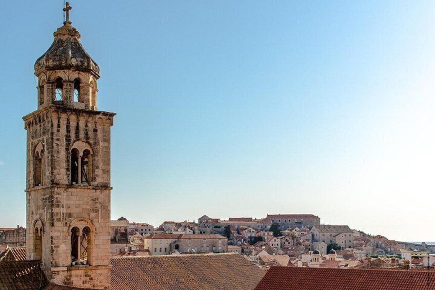 A historic tower with arched windows and a bell, overlooking a town with terracotta rooftops and ancient buildings. 4