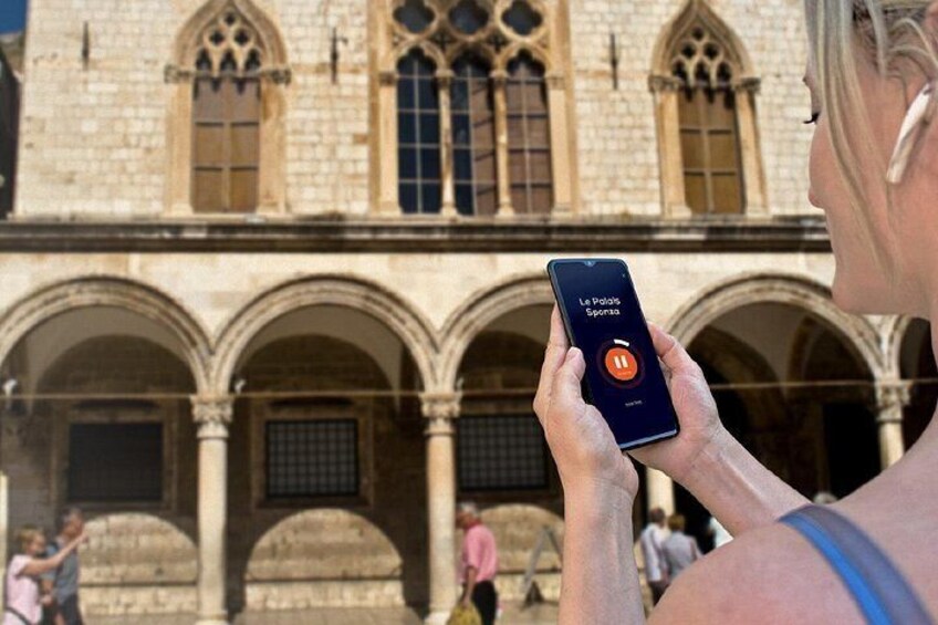 A person using a smartphone with an app interface in front of a historic building with arches. 5