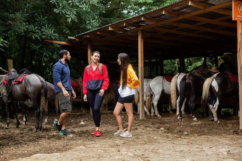 A group of people standing in a stable area with horses. 5