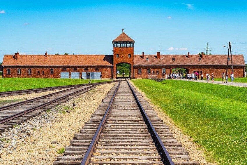 A historical building with a tower, railway tracks, and a grassy area. 4