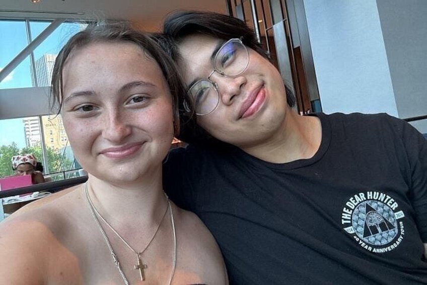 Two people sitting close together, one wearing a black t-shirt with a logo and text, and the other with a necklace and a cross pendant. 4