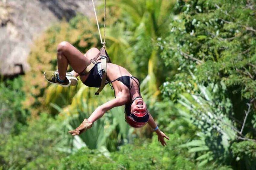 A person in a harness suspended in mid-air, surrounded by lush greenery. 3
