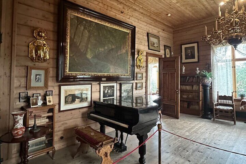 A wooden room with a grand piano, framed pictures, and a chandelier. 3
