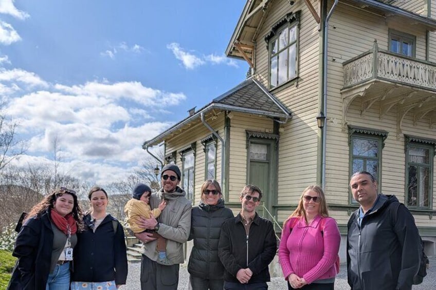 A group of people standing in front of a large, historic house with a balcony. 1
