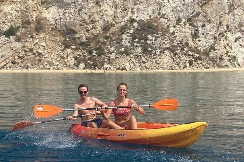 Two people kayaking on a calm body of water with rocky cliffs in the background. 5