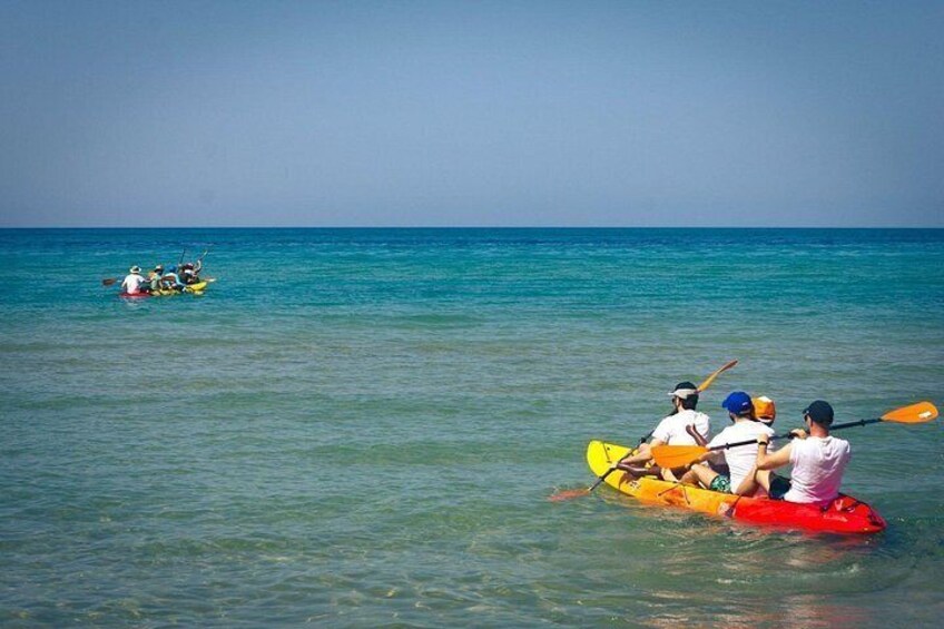 People kayaking on a calm sea, with clear skies and distant boats. 2