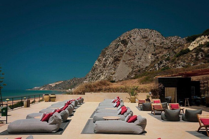 A beachside lounge with sun loungers, a rocky mountain in the background, and a clear sky. 3