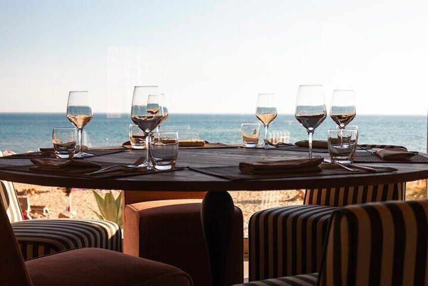 A table set for dining with wine glasses and plates, overlooking a beach. 3