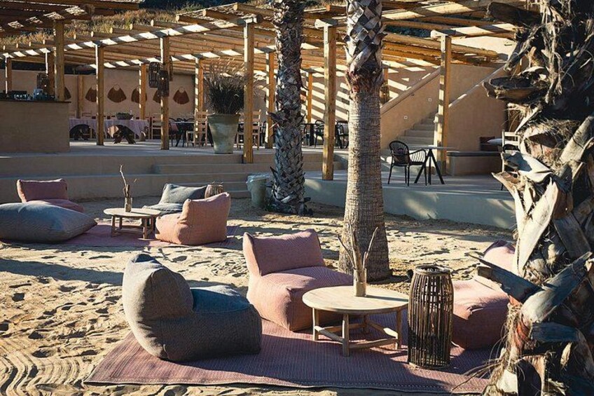 An outdoor seating area with cushioned chairs and tables, palm trees, and a pergola structure. 2