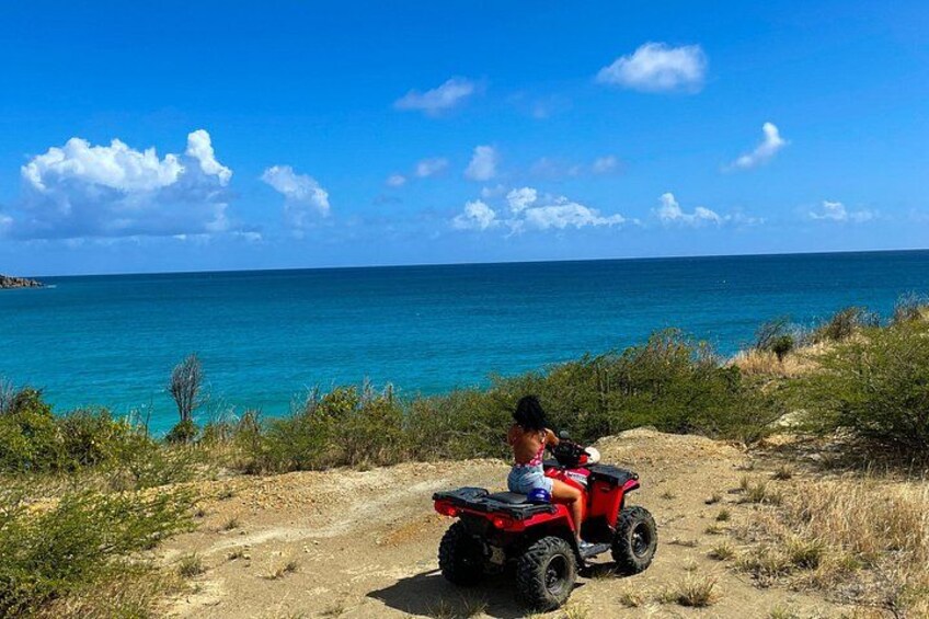 En person kører på en rød ATV på en jordvej tæt ved vand. 4