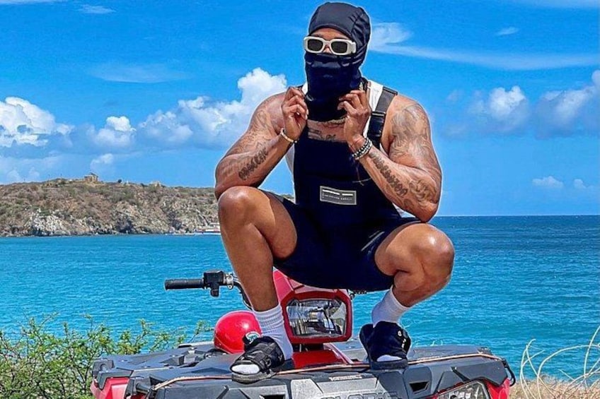 En person sidder på en rød ATV ved vandet under en klar himmel. 3