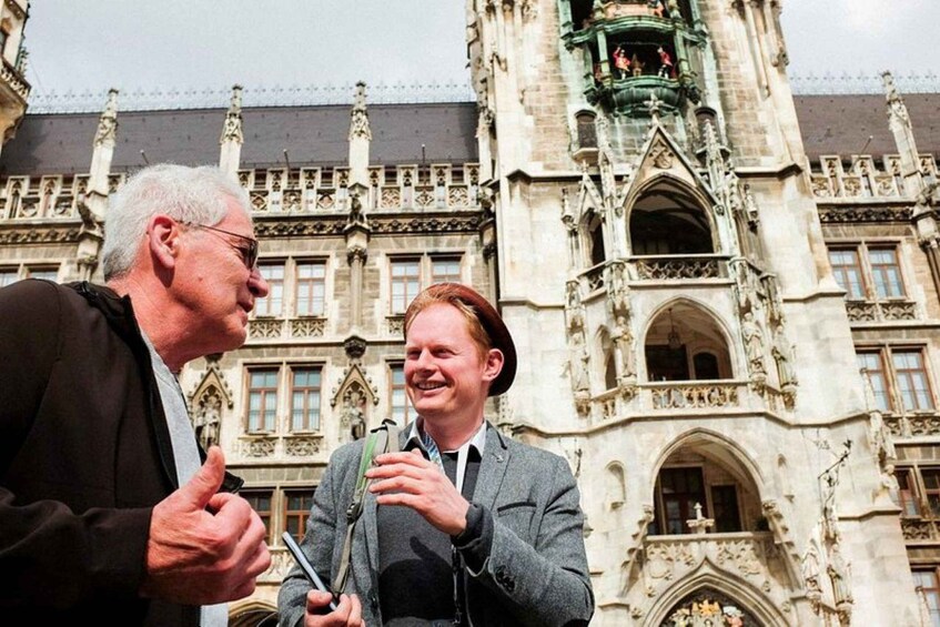Two individuals conversing in front of a historic building with intricate architectural details. 2