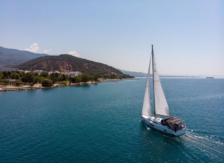 A sailboat on a calm sea with a mountainous coastline in the background. 1