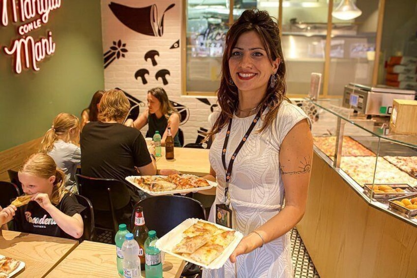 Une personne tenant une part de pizza dans un restaurant, avec un comptoir où sont exposés différents plats. 4