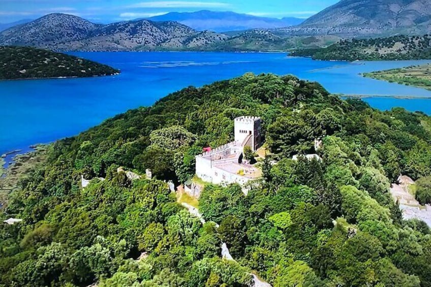A castle on a lush green hill overlooking a large body of water. 1