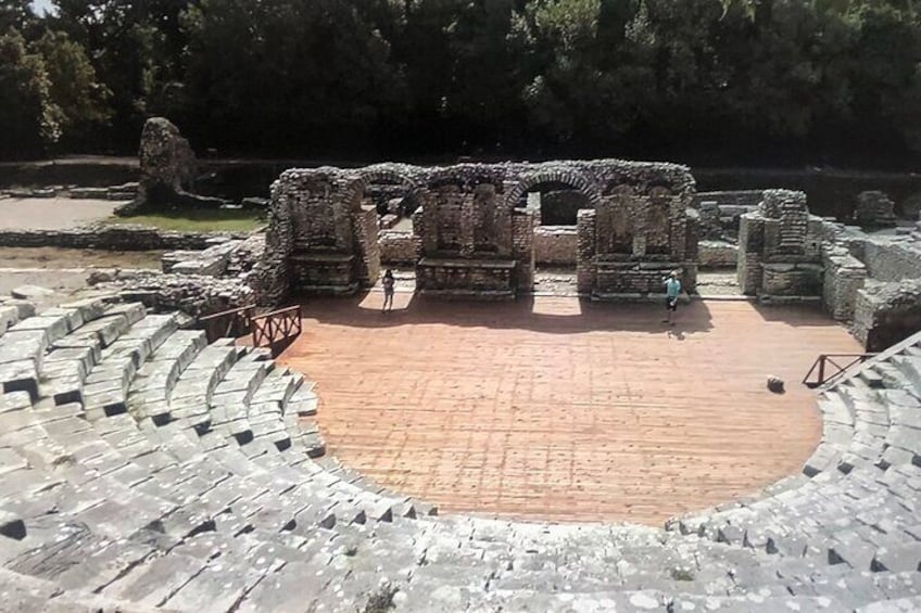 An ancient amphitheater with stone seating and ruins in the center. 2