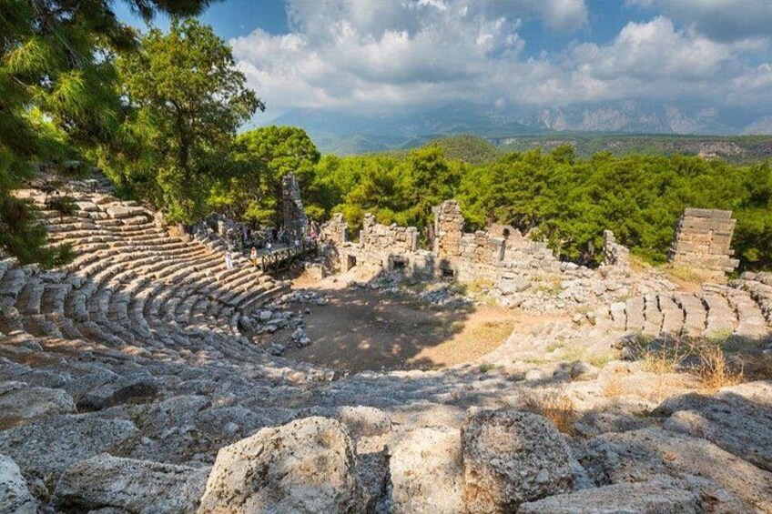 Ancient ruins with a partially intact amphitheater, surrounded by trees and rocky terrain. 3