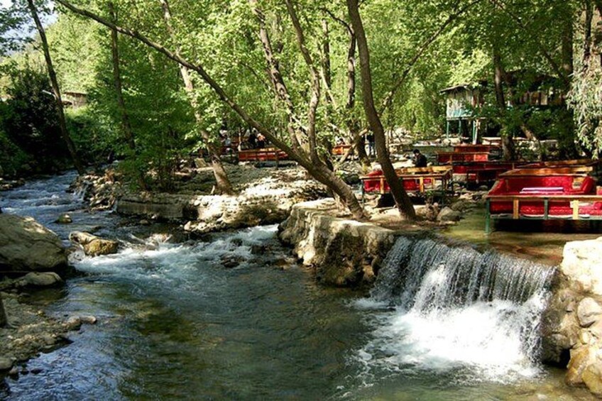 A river with a small waterfall, surrounded by trees and red boats. 2