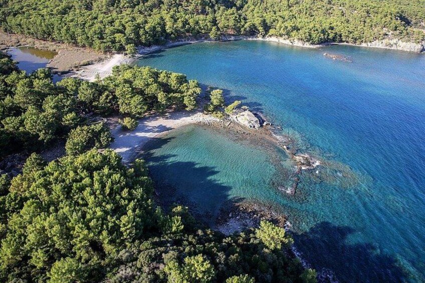 A coastal landscape with clear turquoise waters, dense green forest, and rocky outcrops. 5