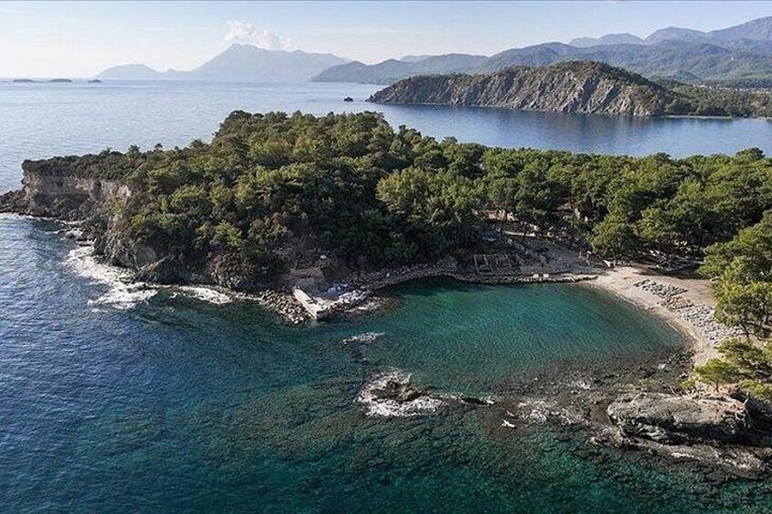 A coastal landscape with a clear blue sea, rocky cliffs, and dense green vegetation. 4