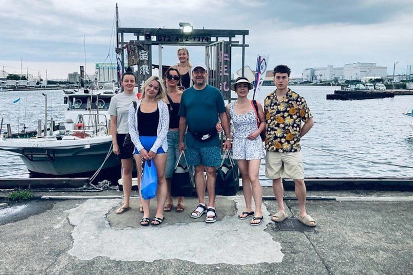 A group of people standing by a waterfront with a boat docked in the background. 1