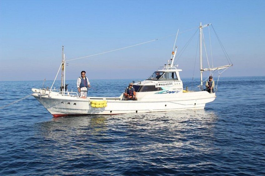 A white fishing boat with two people on deck, one standing and one sitting, on calm blue water. 5
