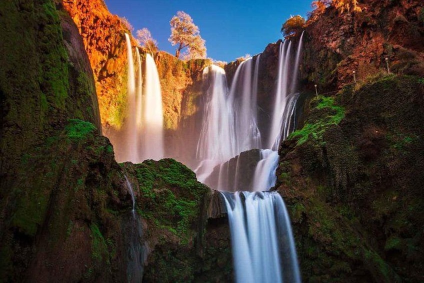 Una cascada se precipita sobre rocas cubiertas de musgo, bajo un cielo despejado. 1