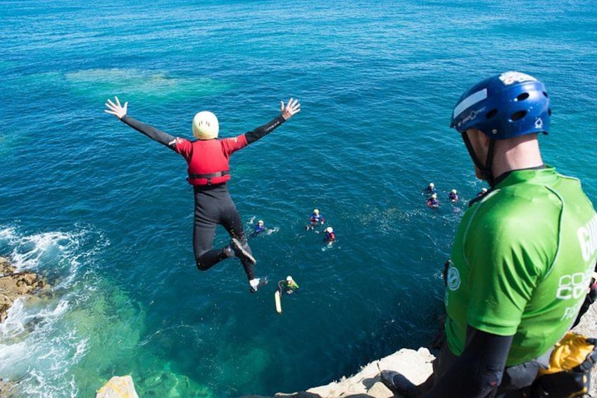 A person jumping into the sea from a cliff, with other people swimming below. 1