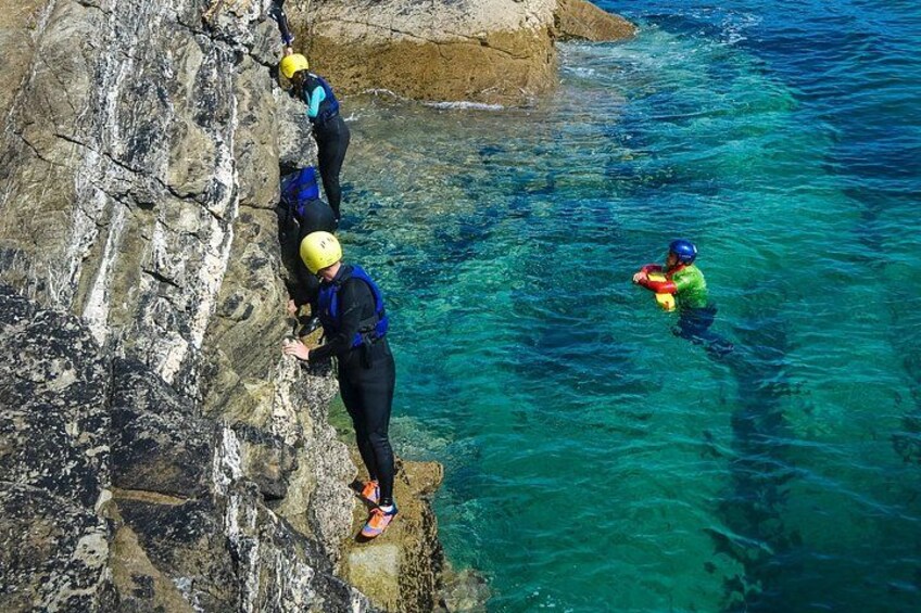 Three people climbing a rocky cliff, with clear blue water below. 2