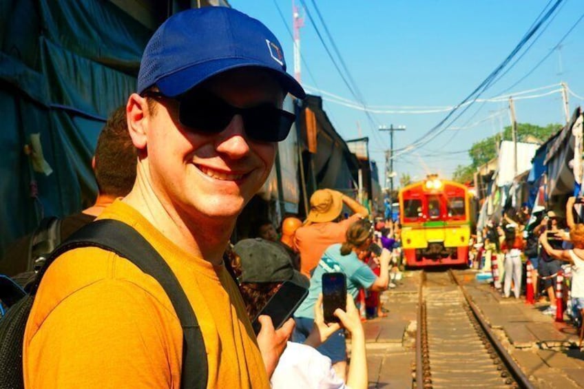 A person in a yellow shirt and blue cap standing on a train track with a train in the background. 3