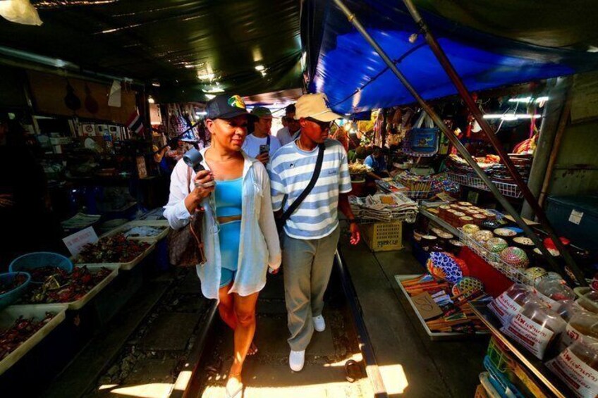 A market with people walking, stalls selling fruits and vegetables, and a blue tarp overhead. 4