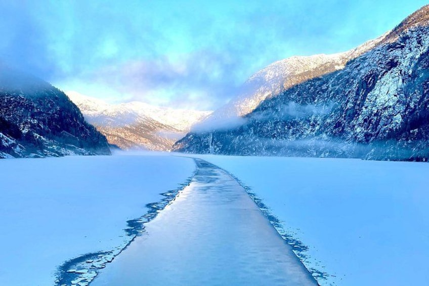 Een bevroren rivier met sneeuwbedekte bergen aan weerszijden. 1